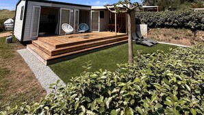 En moderne campingvogn med terrasse, udendørs møbler og en velplejet have.