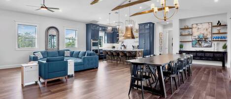 Un grand espace de vie comprenant un canapé bleu, une table à manger avec des chaises et une cuisine équipée d’appareils électroménagers modernes.