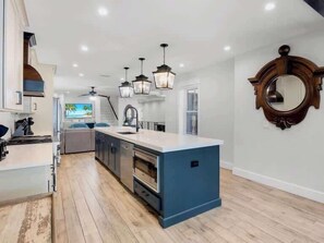 A modern kitchen with a central island, pendant lighting, and a view to a living area. - The Shore House~St Armands, Lido Beach, Pool (Sarasota)