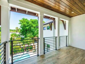 A spacious balcony with a wooden floor, metal railings, and a view of lush greenery. - The Shore House ~ Lido Key ~ Pool/Spa (Sarasota)