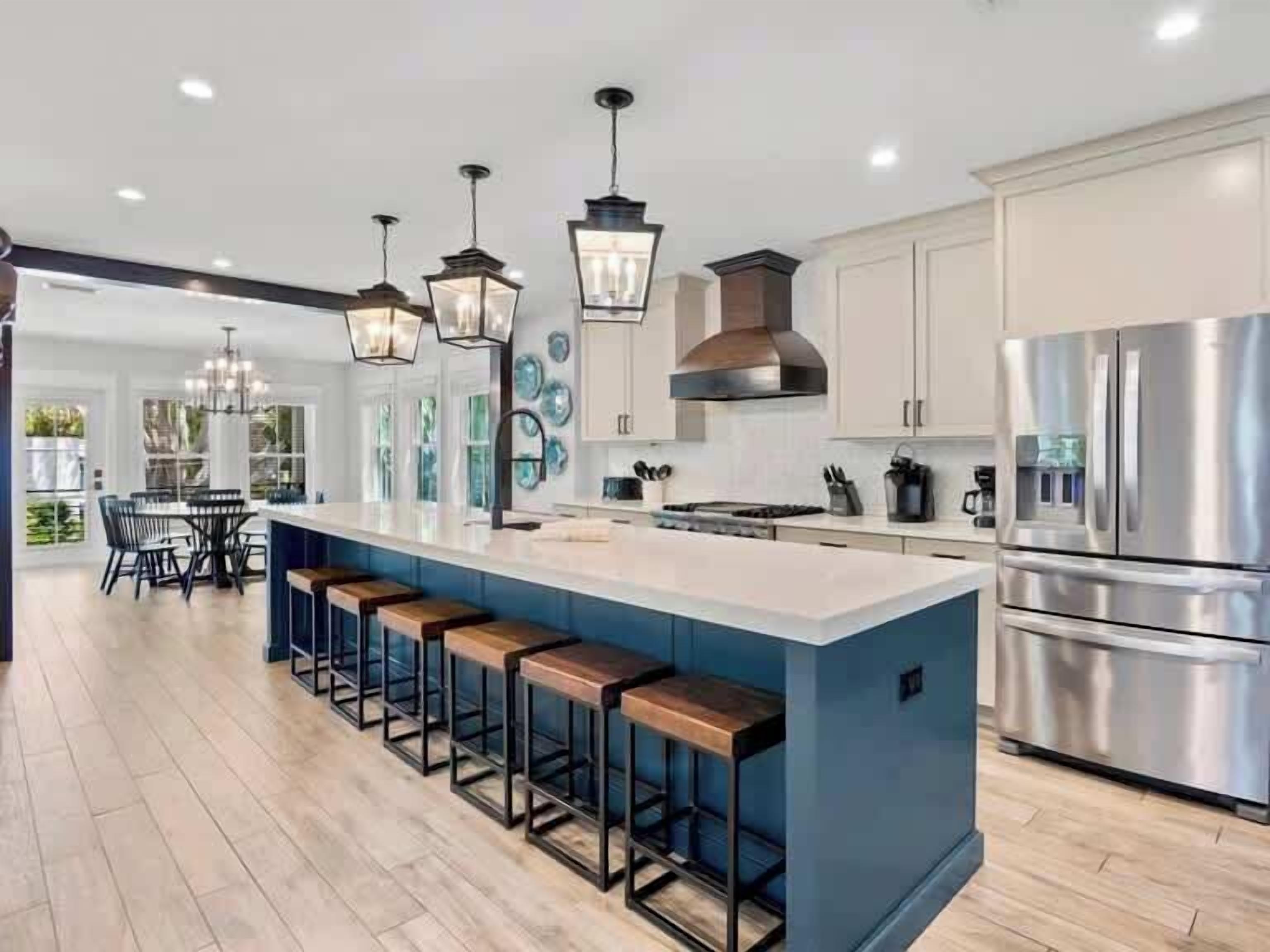 A modern kitchen with a large island, bar stools, stainless steel appliances, and pendant lighting.