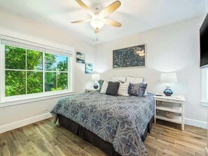 A bedroom with a large bed, a ceiling fan, a window with a view of greenery, and a wall-mounted TV. - The Shore House~St Armands, Lido Beach, Pool (Sarasota)