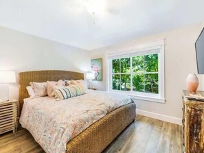 Une chambre avec un grand lit, une fenêtre donnant sur un paysage verdoyant et une tête de lit en osier.