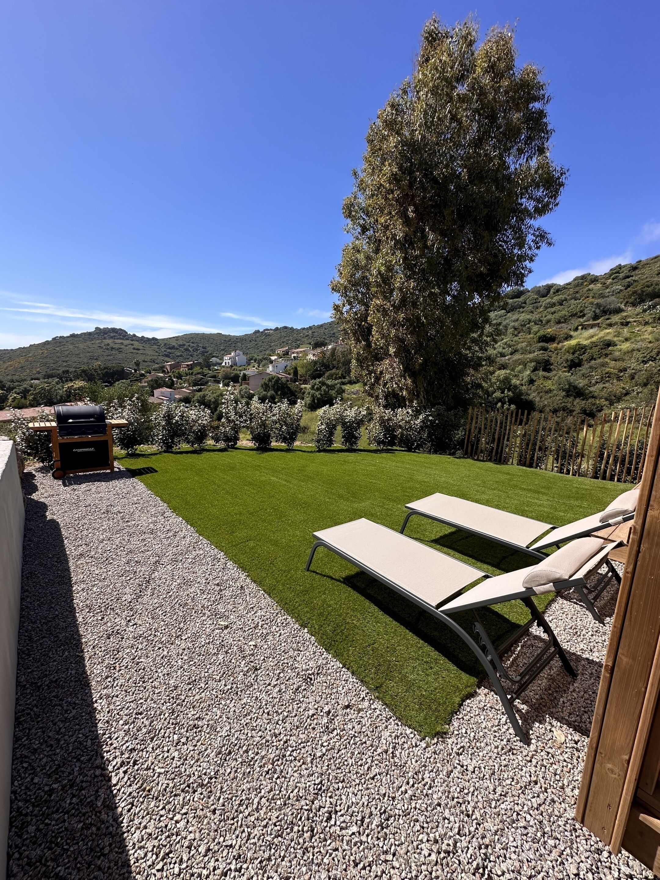 Un patio con dos sillones de descanso, una parrilla y un césped bien cuidado.