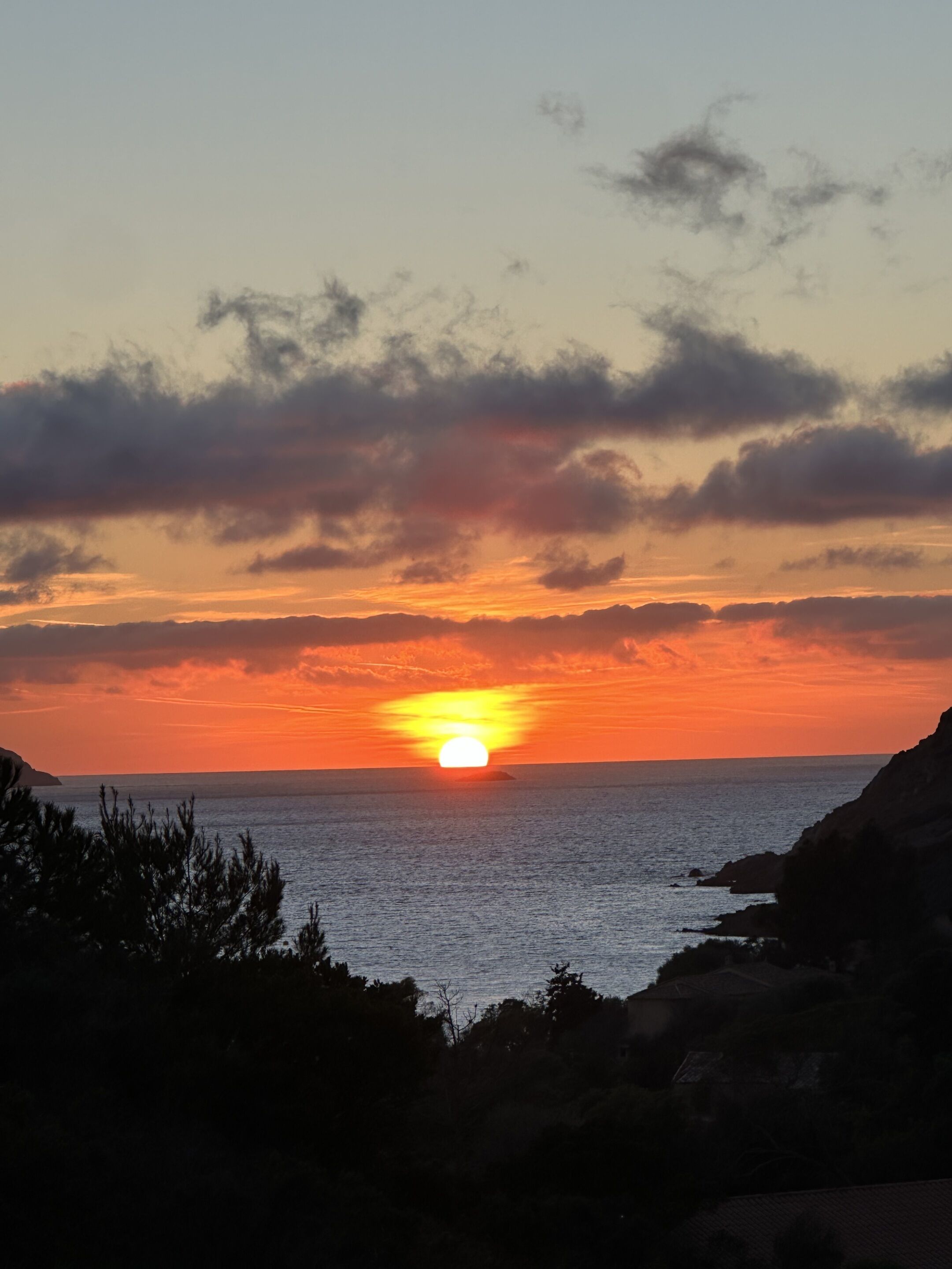A sunset over a coastal landscape with a view of the sea and distant land.