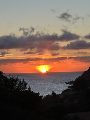 A sunset over a coastal landscape with a view of the sea and distant land.