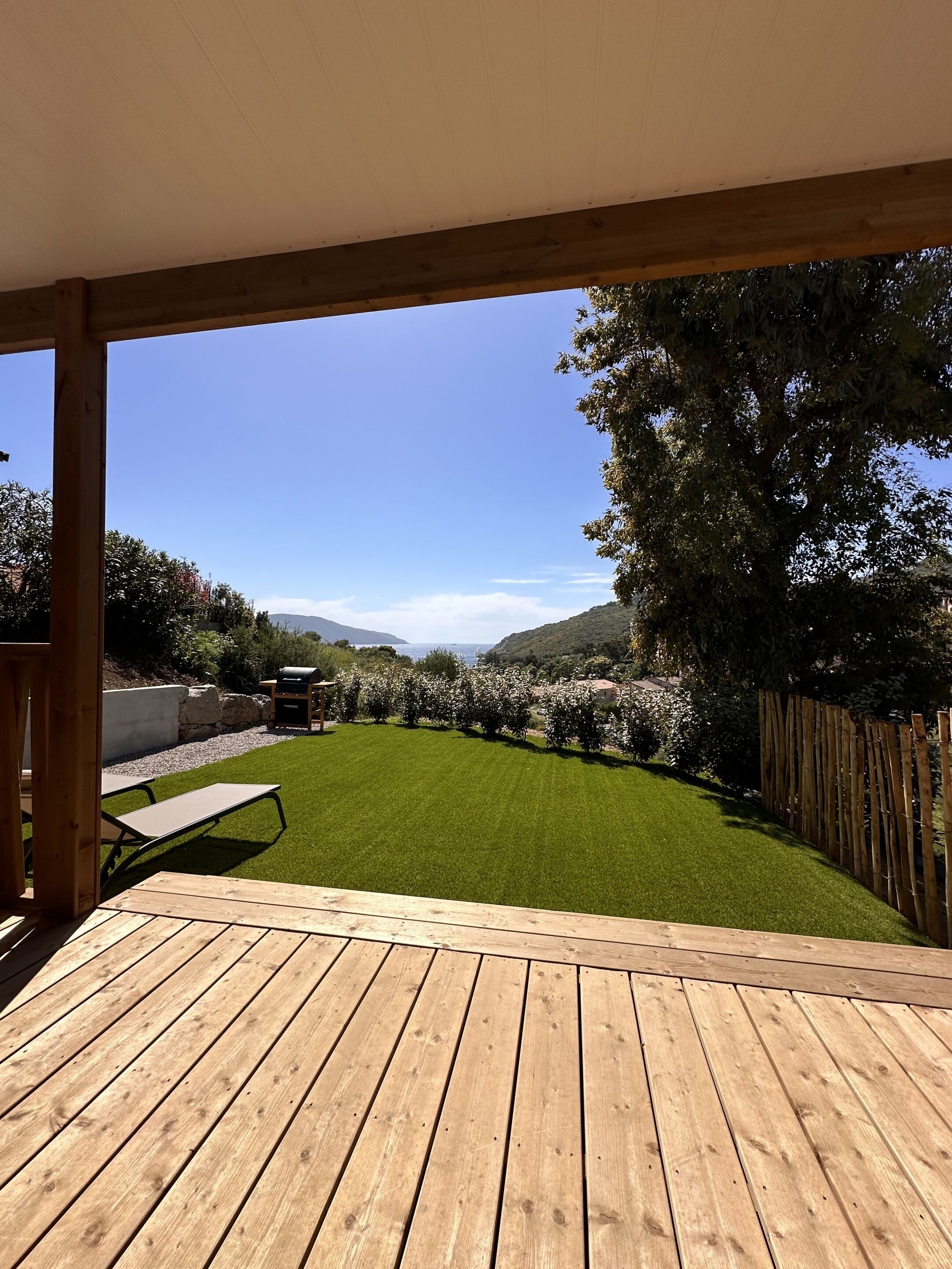 A wooden deck with a view of a well-maintained lawn and a stone wall.