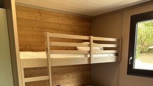 A bunk bed with a wooden headboard and a single bed below. There is a window with a view of greenery outside. - Porto Chalet - Cozy & Modern, Sleeps 6 (Appietto)