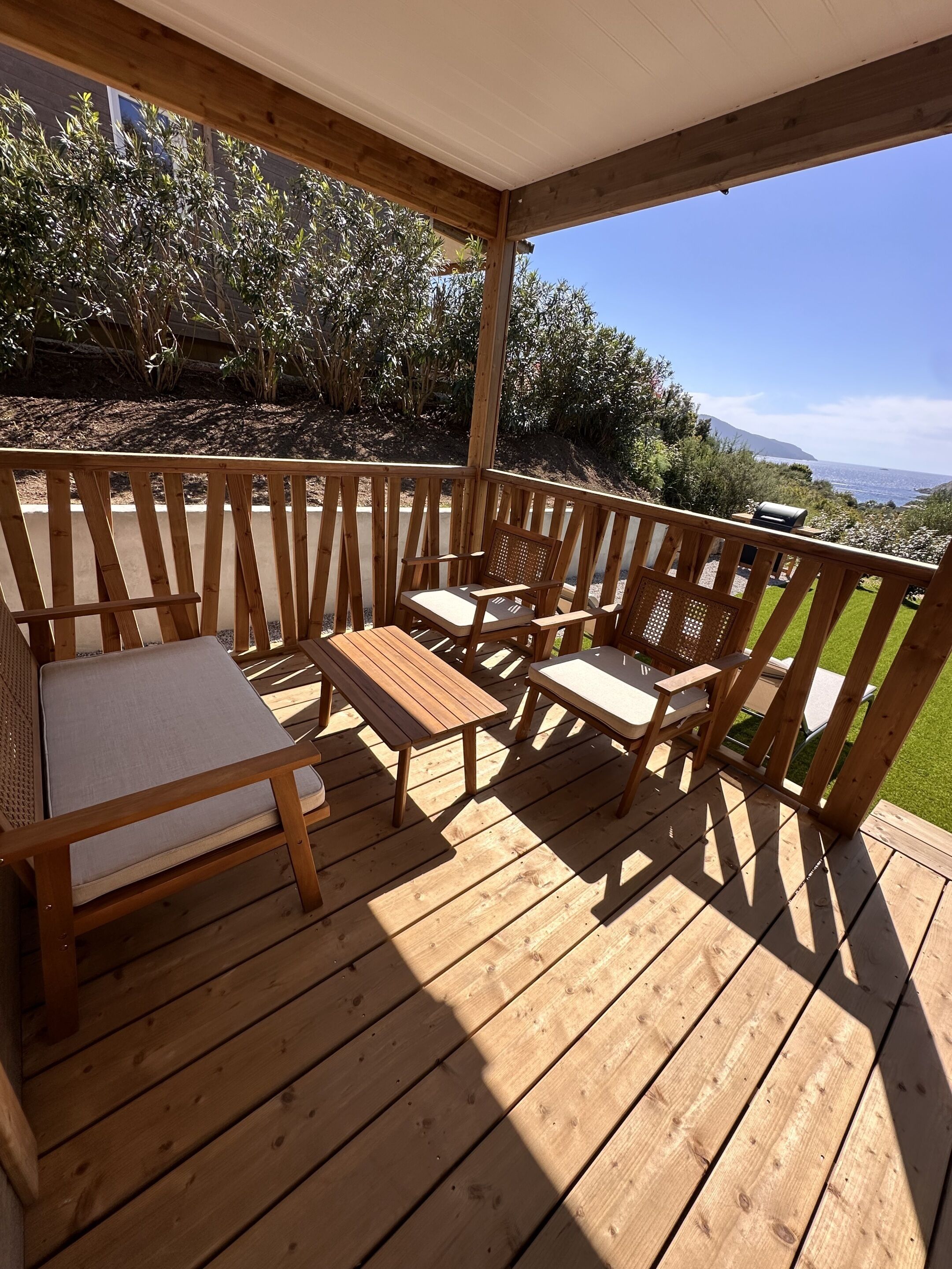 A wooden deck with outdoor furniture, including a sofa and chairs, overlooking a landscape with trees and a distant view.