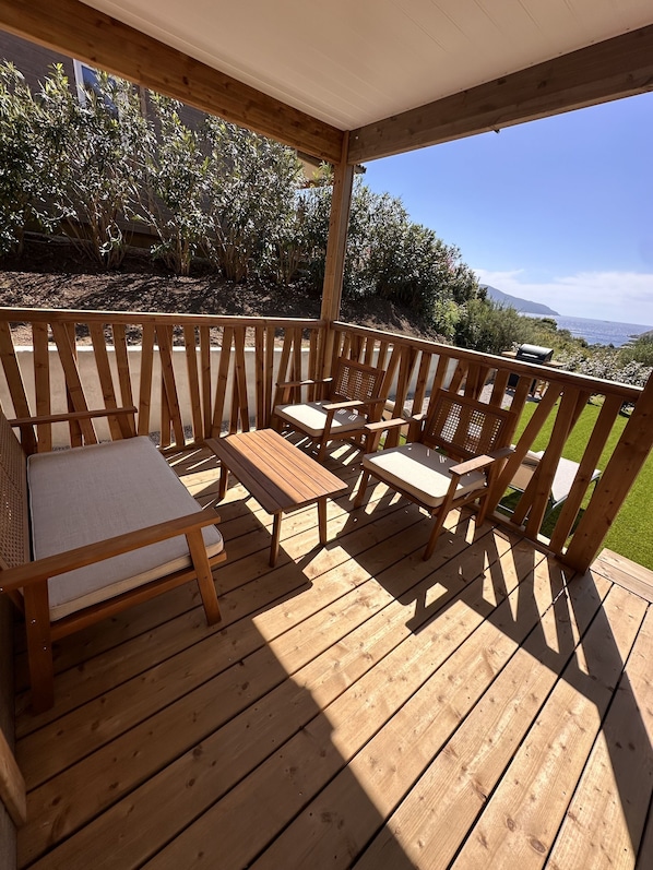 A wooden deck with outdoor furniture, including a sofa and chairs, overlooking a landscape with trees and a distant view.