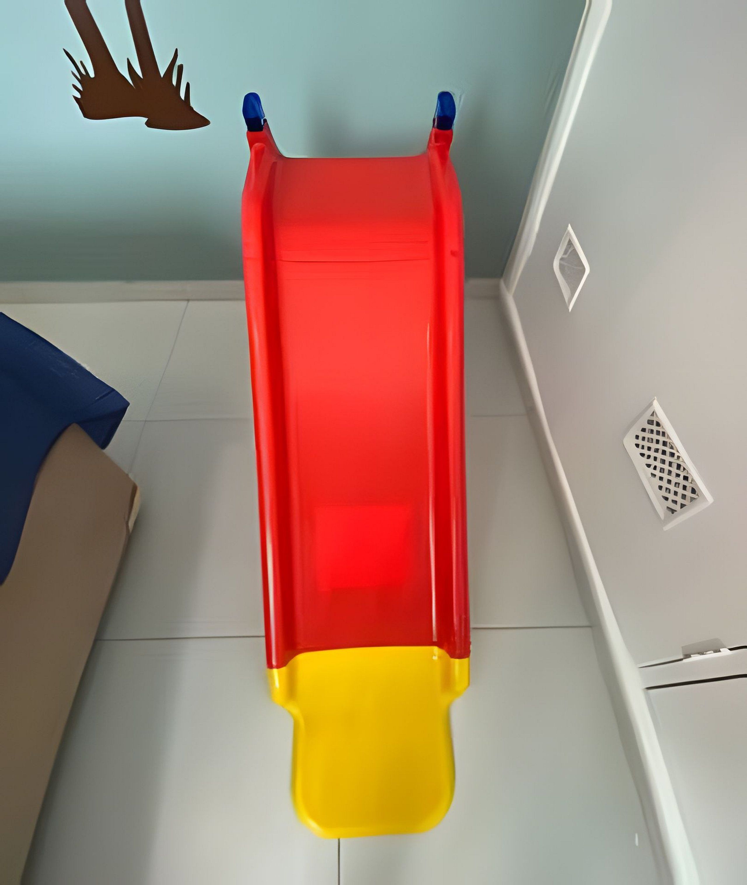 Un tobogán rojo y amarillo en una habitación con suelo de baldosas y pared azul.