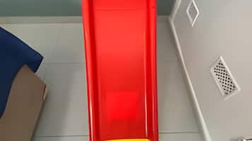 Un tobogán rojo y amarillo en una habitación con suelo de baldosas y pared azul.