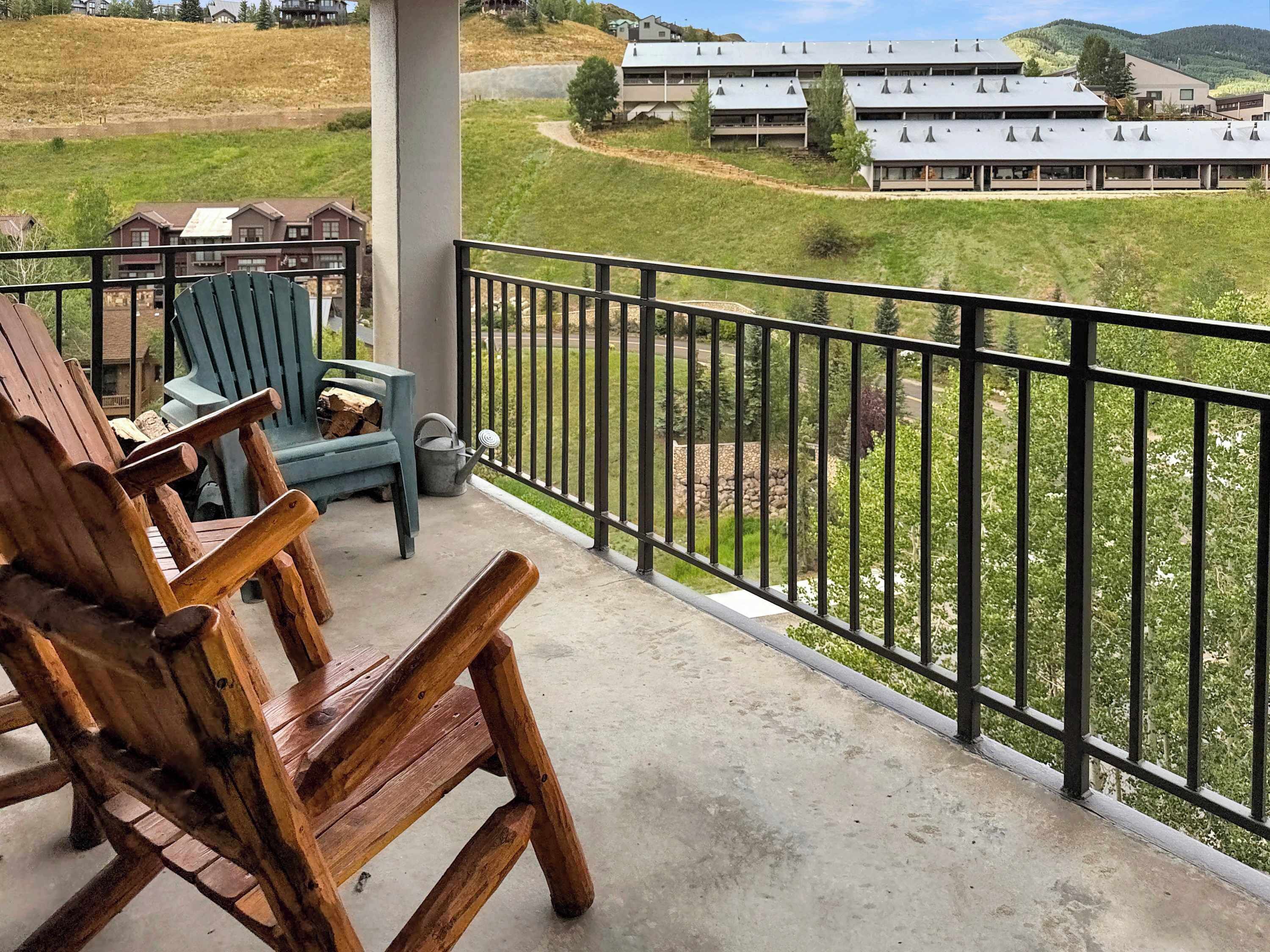 Ein Balkon mit Holzstühlen und einem Betonboden, der auf eine grüne Landschaft mit Gebäuden im Hintergrund blickt.