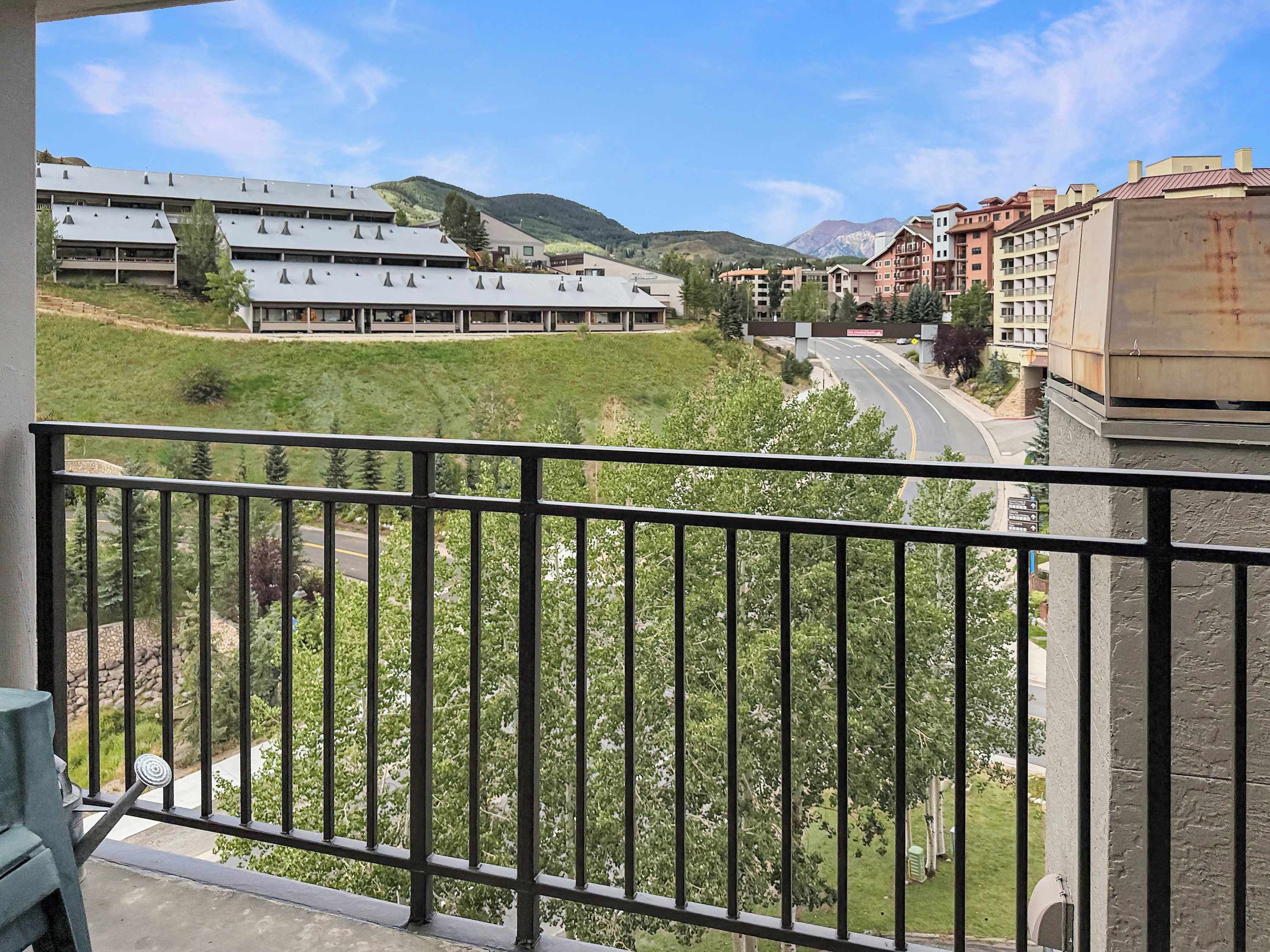 A balcony with a view of a road, buildings, and a hilly landscape.