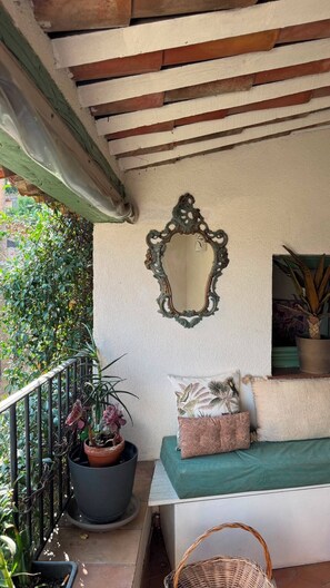 Ein Balkon mit einem Blumentopf, einem Zier-Spiegel und einer gepolsterten Bank.
