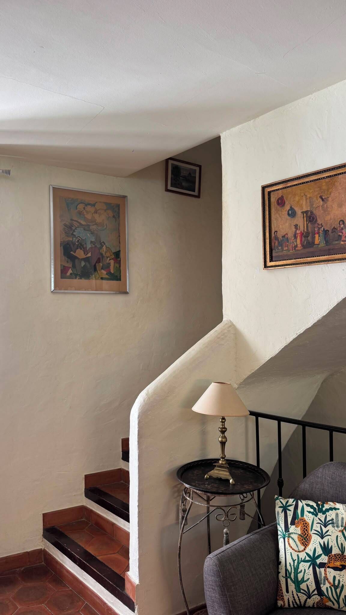 A staircase with a lamp and a chair, a painting on the wall, and a small framed picture above the lamp.