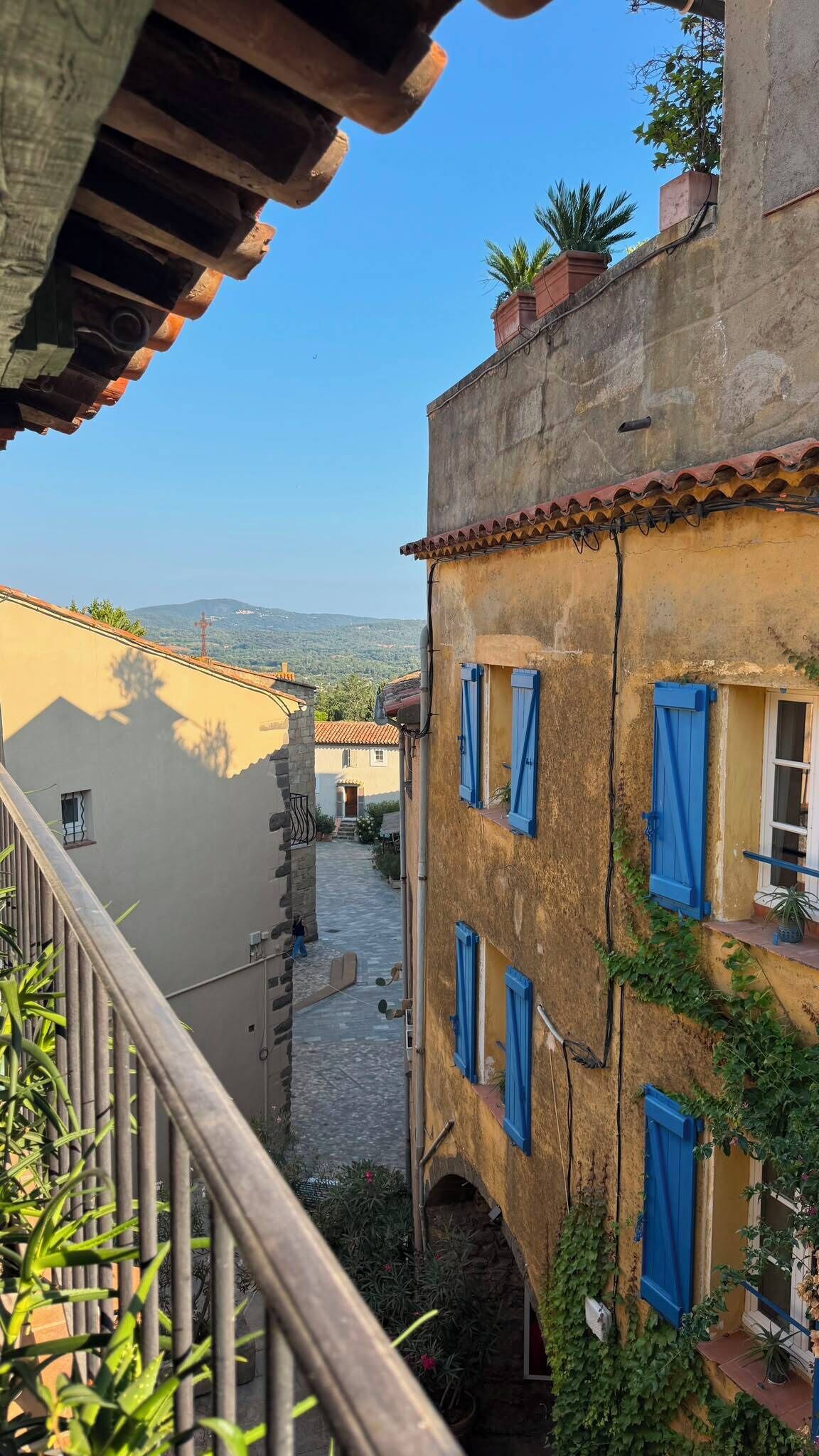Une ruelle étroite, bordée de bâtiments des deux côtés, avec un escalier bien visible et une vue dégagée sur le paysage environnant.