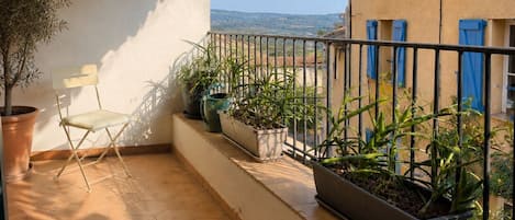 A balcony with a tiled floor, potted plants, a folding chair, and a wicker basket.