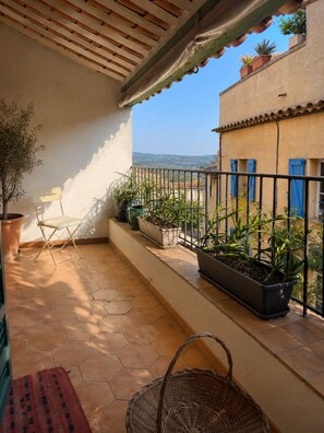 A balcony with a tiled floor, potted plants, a folding chair, and a wicker basket. - L'Oustalet Maelvi – In the medieval heart of Grimaud, 50 meters from the castle and the church (Grimaud)