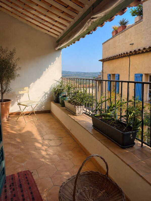A balcony with a tiled floor, potted plants, a folding chair, and a wicker basket.