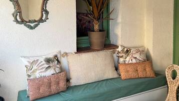 Un coin salon accueillant avec un banc, des coussins, un miroir, une plante en pot et une lanterne suspendue.