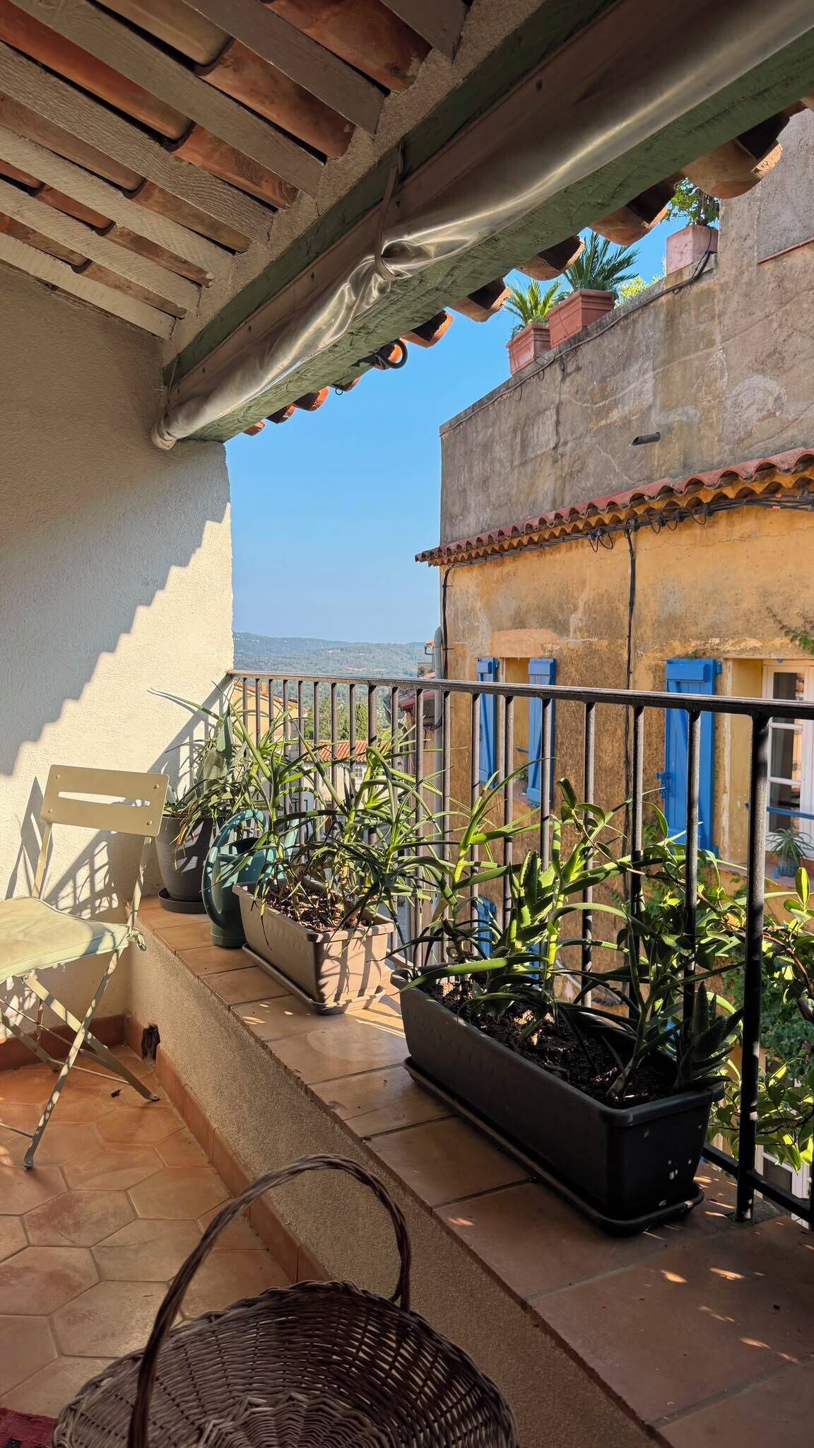 A balcony with a chair, potted plants, and a view of a cityscape.
