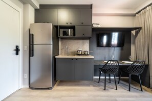 A compact kitchen with a refrigerator, microwave, and stove, a dining area with chairs, and a flat-screen TV mounted above the counter. - GA 45 Ape com AR prox. Allianz  (São Paulo)