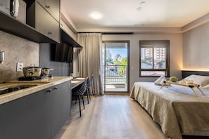 A compact hotel room with a kitchenette, a balcony with a city view, and a bed with a tray of breakfast. - GA 45 Ape com AR prox. Allianz  (São Paulo)