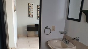 A bathroom with a toilet, sink, and a mirror. There is a door leading to another room.
