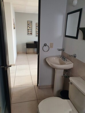A bathroom with a toilet, sink, and a mirror. There is a door leading to another room.