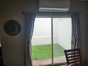 Ein Zimmer mit einer Schiebetür zum Balkon, der mit Kunstgrün gestaltet ist, einer Wandklimaanlage und einer Wanduhr.