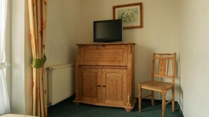 A room with a wooden cabinet, a television on top, a chair, a radiator, and a framed picture on the wall.