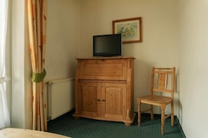 A room with a wooden cabinet, a television on top, a chair, a radiator, and a framed picture on the wall.