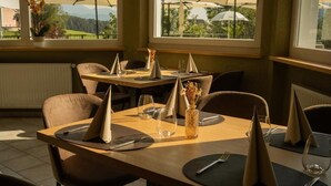 A restaurant with tables set for dining, chairs, and a view of the outdoors.