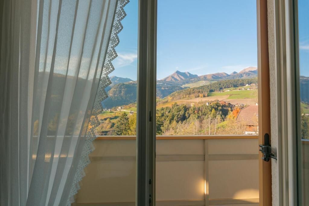 Ein Zimmer mit Blick auf eine gebirgige Landschaft durch ein Fenster mit einer Spitzenvorhang.