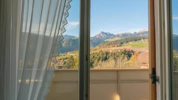 Ein Zimmer mit Blick auf eine gebirgige Landschaft durch ein Fenster mit einer Spitzenvorhang.