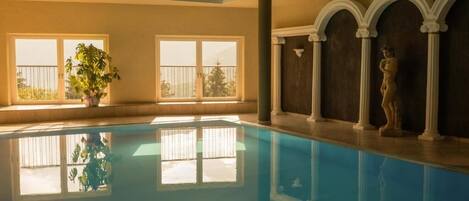 A swimming pool with clear water, large windows, and a statue on the right.