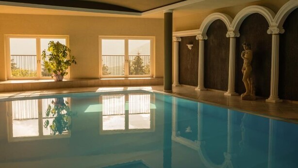 A swimming pool with clear water, large windows, and a statue on the right.