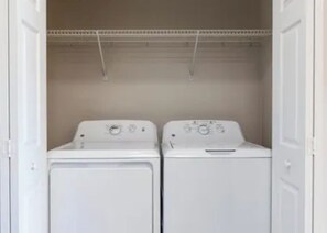 A laundry room with two white washing machines and a metal shelving unit above. - Minutes from Disney! Resort Living at its Finest (Kissimmee)