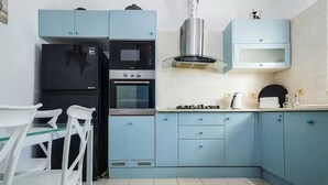 Una cocina con armarios azules, un refrigerador negro, una estufa y sillas blancas.
