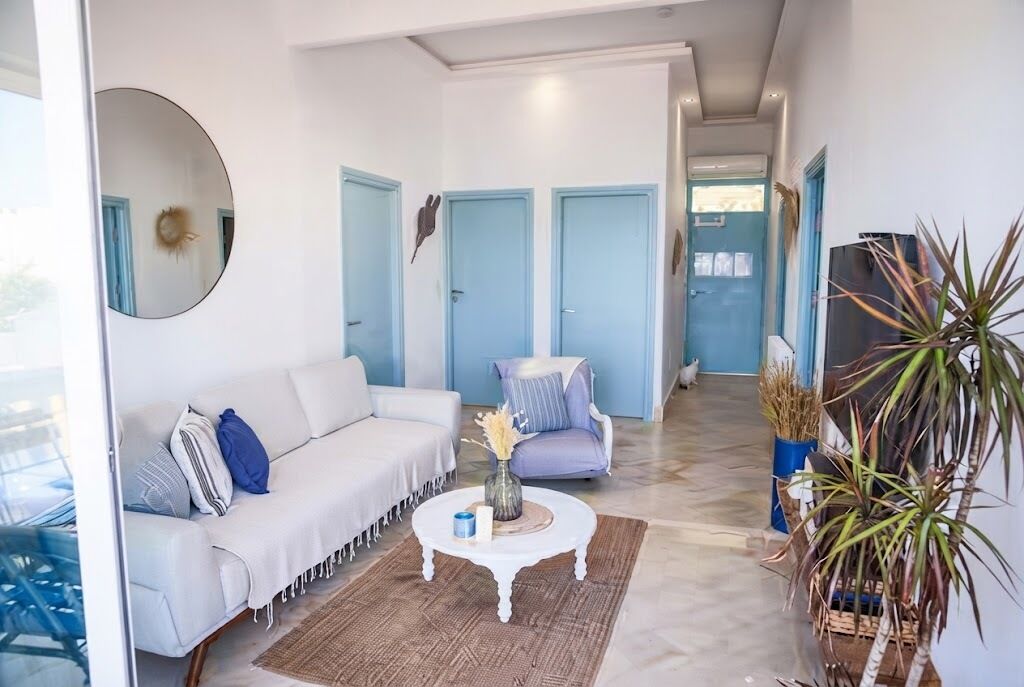 A modern living room with a white sofa, a round coffee table, and a blue chair. There are two blue doors in the background.