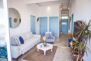 Een moderne woonkamer met een witte bank, een ronde salontafel en een blauwe fauteuil. Achtergrond toont twee blauwe deuren.
