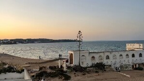 Escena costera con un edificio de fachada blanca y ventanas de arco.