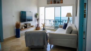 Un salón moderno con sofá, televisor y balcón con vistas al mar.