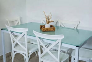 Een eetgedeelte met een tafel met glazen blad en witte stoelen.