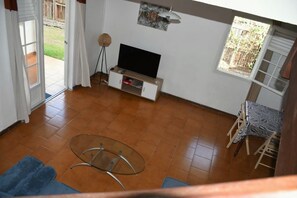 Ein Wohnzimmer mit Fernseher, einem Glastisch, einer Couch und einem Essbereich mit Tisch und Stühlen.