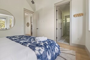 Ein Schlafzimmer mit einem großen Bett, einem Spiegel, einer Tür zu einem Badezimmer und Blick ins Freie.
