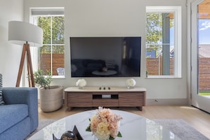 Ein stilvolles Wohnzimmer mit Flachbildfernseher, einer Couch, einem Couchtisch mit Blumen und einer Stehlampe.