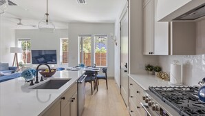 A modern kitchen with a central island, a dining area with blue chairs, and a view of the outdoors through large windows. - Tremendous 9-bedroom Luxury Compound - Two Pools & Two Houses (Austin)