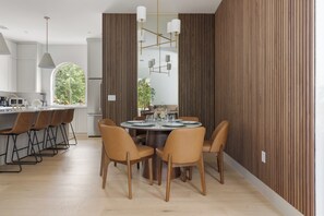 Eine moderne Küche mit weißen Schränken, eine Essecke mit rundem Tisch und Stühlen sowie ein großes Fenster mit Blick auf Grünflächen.